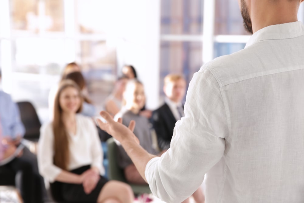 Homem dando palestra e articulando para algumas pessoas à sua frente.