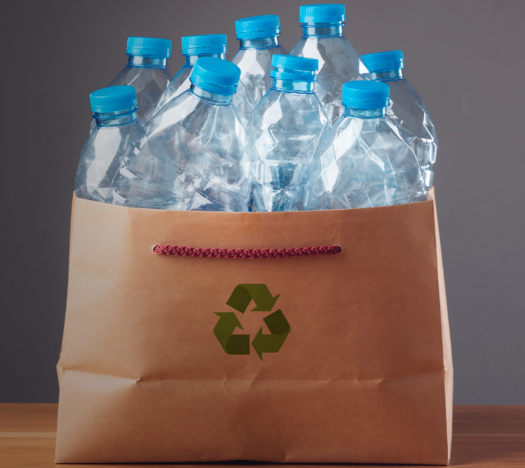 Sacola de papél com ícone de reciclagem com garrafas plásticas dentro.