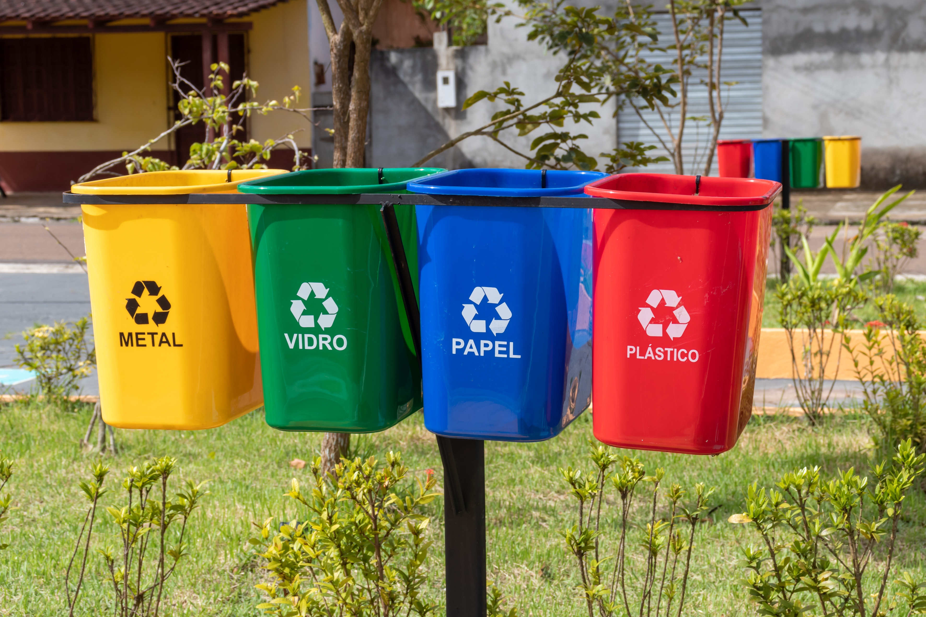 Quatro baldes de lixo com cores específicas e escrita dos materiais adequados.